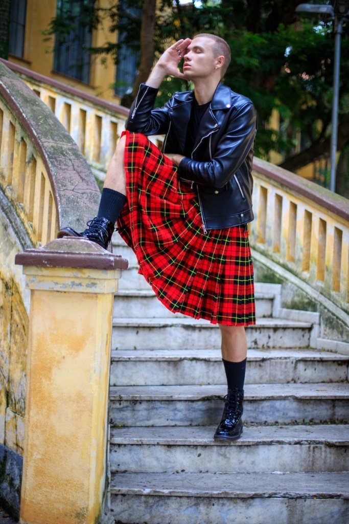 Full body sensual male model in leather jacket and red tartan kilt standing on aged stairs